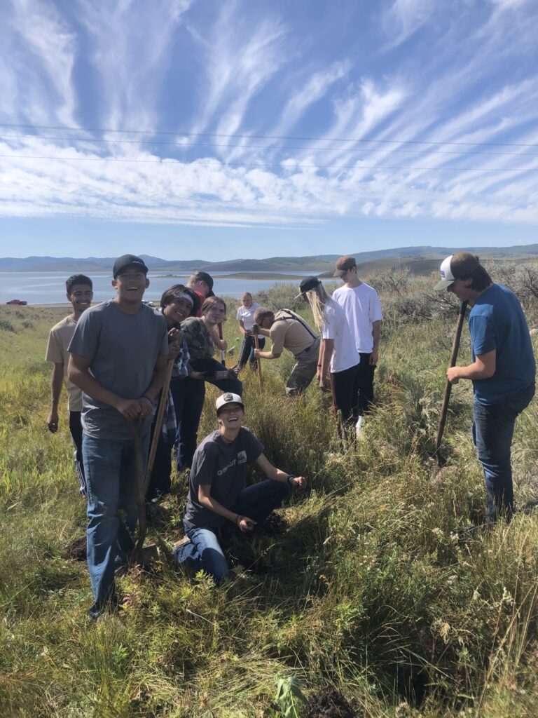 High school students stopping to smile for the camera as they plant trees in a wildlife management area