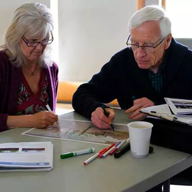 Two older adults using markers to color on a tree coloring page.