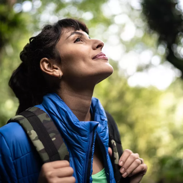 Woman surrounded by trees smiling and breathing fresh air .