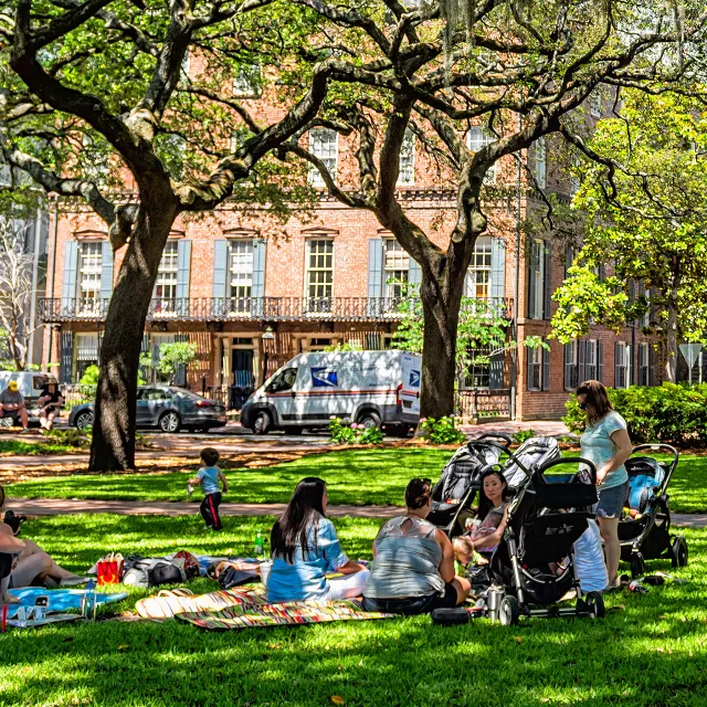 Neighborhood residents gather in a park under the shade of trees.