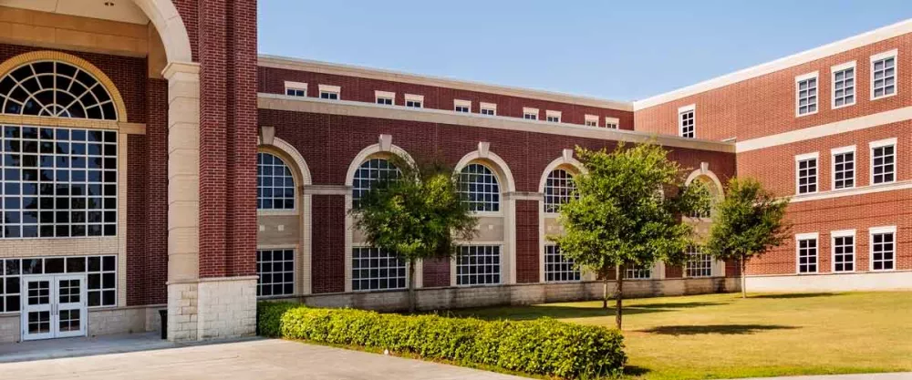 A large brick high school building with multiple windows surrounded by a lush grassy area, creating a welcoming outdoor space.