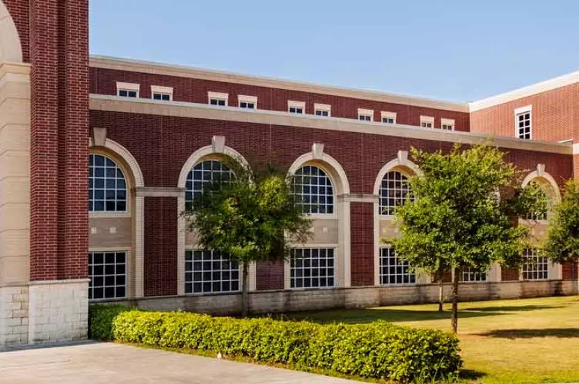 A large brick high school building with multiple windows surrounded by a lush grassy area, creating a welcoming outdoor space.